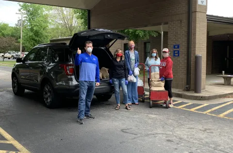 People in face masks stand behind an SUV that they're loading with sacks of food.
